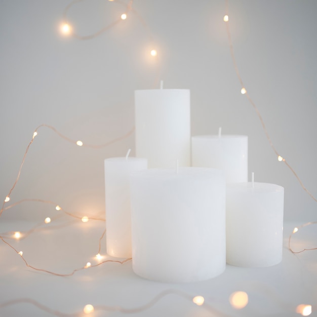 Illuminated fairy lights around white candles on grey background