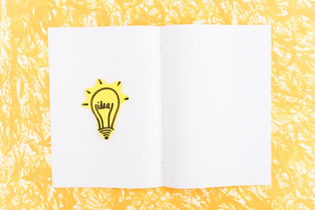 Illuminated idea light bulb drawn on white page over the yellow background