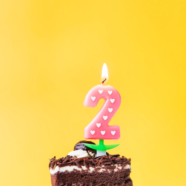 Illuminated love two year candle on cake slice over yellow background