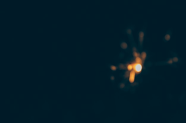 Illuminated sparkler on blurry black backdrop