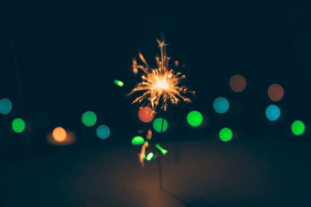 Illuminated sparkler on colorful bokeh background