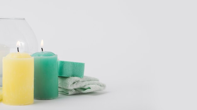 Illuminated yellow and green candles with sponge and napkin isolated on white background