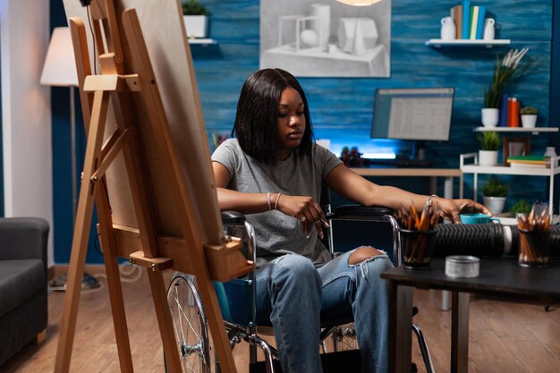 プロのグラフィック鉛筆を使用してキャンバスにスケッチを描く創造的なmasterpriceで作業している障害を持つイラストレーターアーティスト。車椅子スケッチイラストの若い女性。創造性の概念