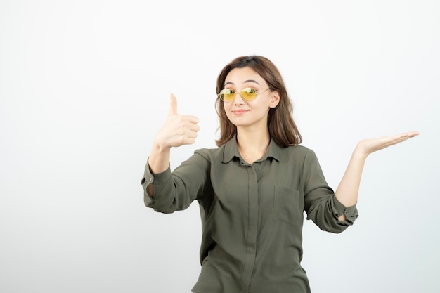 Image of adorable girl in glasses giving thumbs up over white. High quality photo