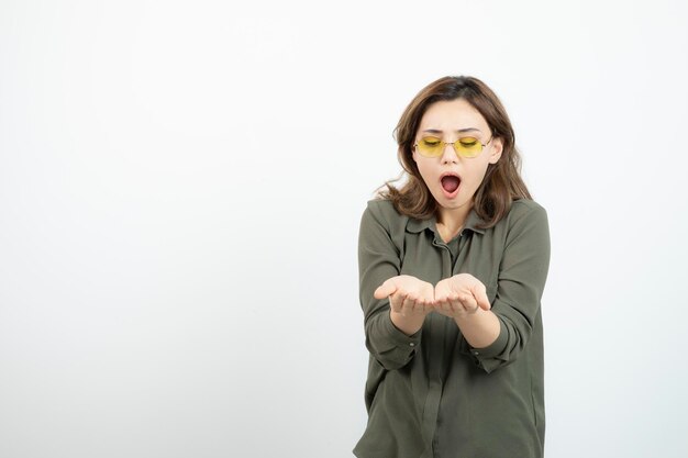 Image of adorable girl in glasses opening her palms over white. High quality photo