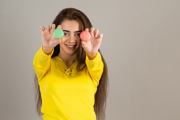 Image of adorable girl holding colorful macaroons on gray wall.