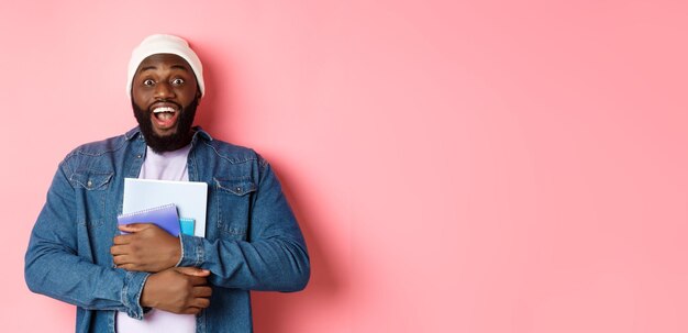 Image of adult africanamerican man holding notebooks and smiling studying at courses standing over p