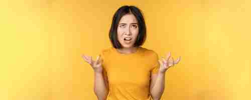 Free photo image of angry asian woman shouting and cursing looking outraged furious face expression standing over yellow background