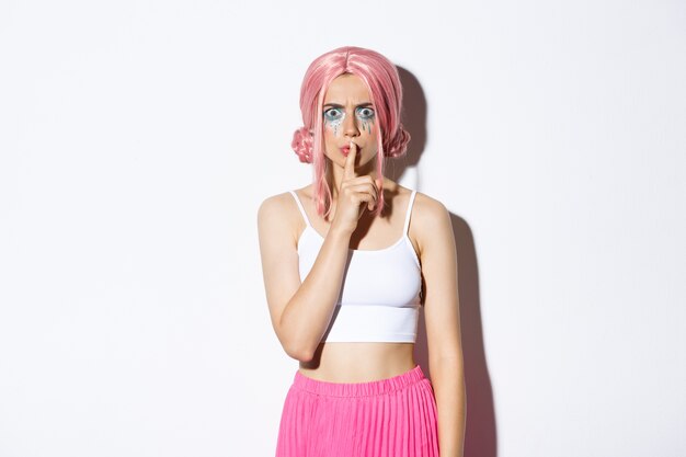 Image of angry frowning girl in pink wig and halloween makeup, shushing at someone, scolding person for being too loud, standing.