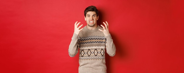 Immagine di un uomo arrabbiato e frustrato in maglione invernale che grida e guarda con odio in piedi sconvolto