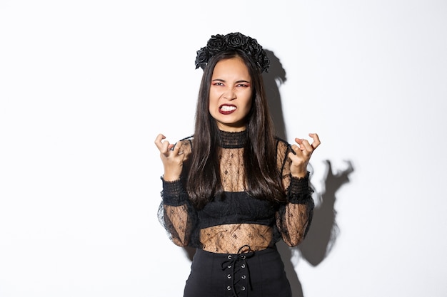 Free photo image of angry wicked witch cursing and swearing, clenching fists and grimacing with hatred, standing over white background, celebrating halloween.