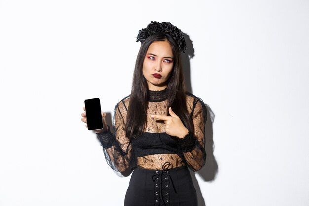 Image of annoyed and reluctant asian girl in witch costume