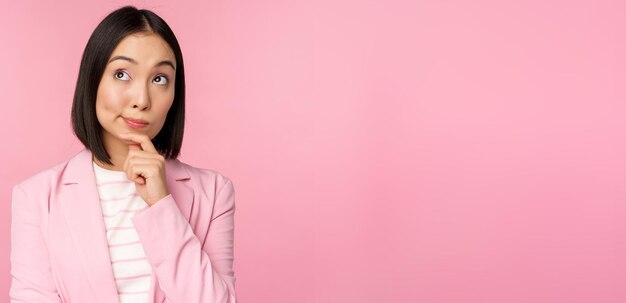image of asian businesswoman standing in thinking pose brainstoming wearing suit korean saleswoman entrepreneur posing against pink background