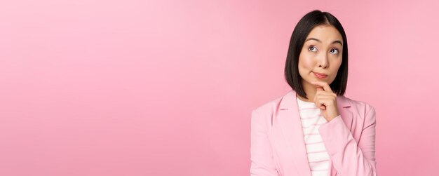 분홍색 배경에 포즈를 취한 한국 판매원 기업가가 정장을 입고 브레인스토밍 포즈를 취하고 있는 아시아 여성 사업가의 이미지
