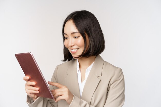 Image of asian businesswoman using digital tablet looking at gadget and smiling working standing against white background