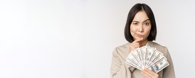 お金の現金ドルを示し、白い背景の上にスーツに立って考えているアジアの企業の女性幸せな実業家の画像