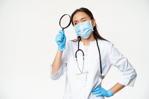 Изображение азиатской женщины-врача, врача с увеличительным стеклом, медицинской маски и резиновых перчаток для обследования пациента, белый фон.