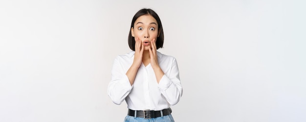 Image of asian female model looking surprised staring amazed reacting at surprise big news standing over white background