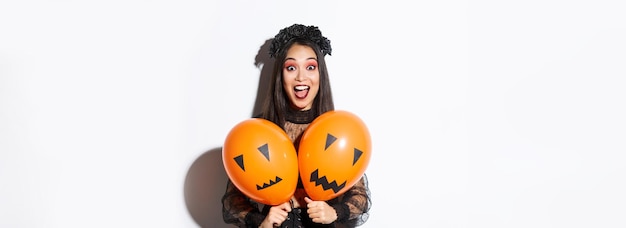 Free photo image of asian girl in evil witch costume holding two orange balloons with scary faces celebrating h