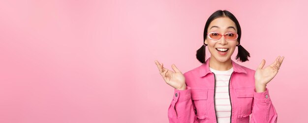 Image of asian girl looking surprised and excited smiling amazed reaction to big news standing over pink background