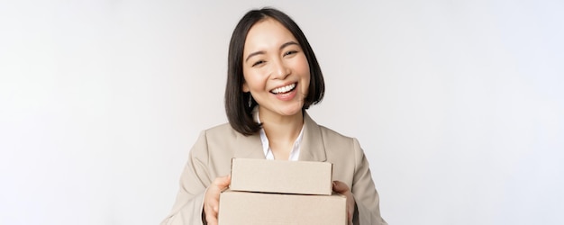 주문과 함께 상자를 제공하는 아시아 판매원 비즈니스 여성의 이미지는 배경 위에 정장을 입은 고객에게 배달됩니다.