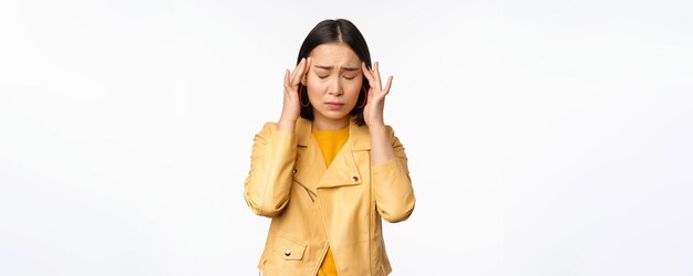 흰색 배경 위에 서 있는 두통 편두통을 앓고 있는 걱정스러운 얼굴로 머리 관자놀이를 마사지하는 아시아 여성의 이미지
