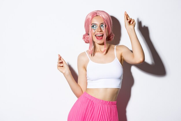 Image of attractive party girl with pink wig and bright makeup, having fun and celebrating holiday, dancing happy.