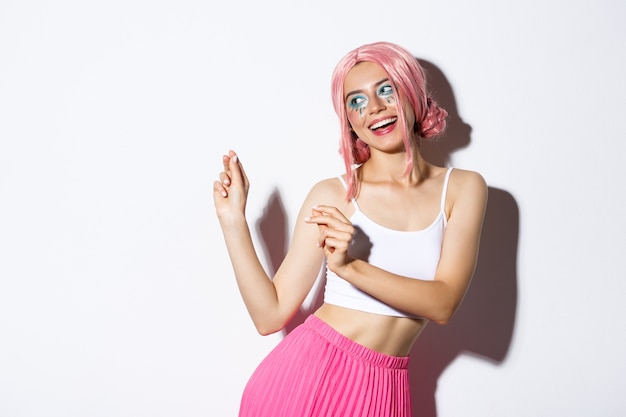 Image of attractive party girl with pink wig and bright makeup, having fun and celebrating holiday, dancing happy.