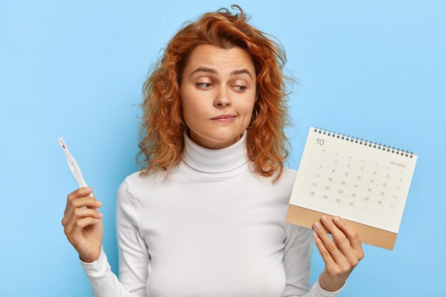 Image of attractive woman holds pregnancy test and periods calendar