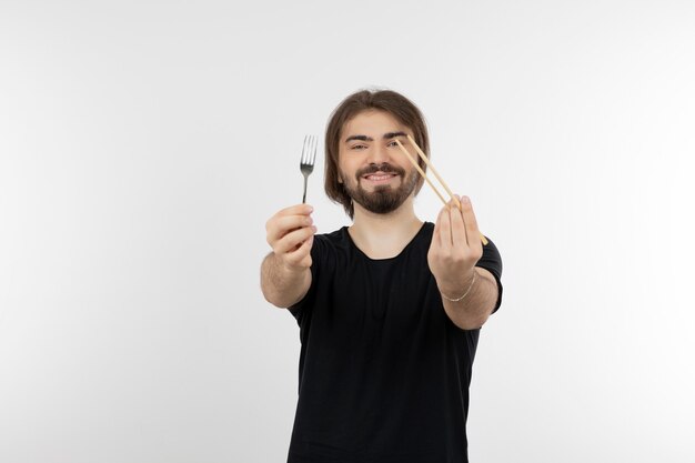 Image of bearded man holding fork over a white wall.