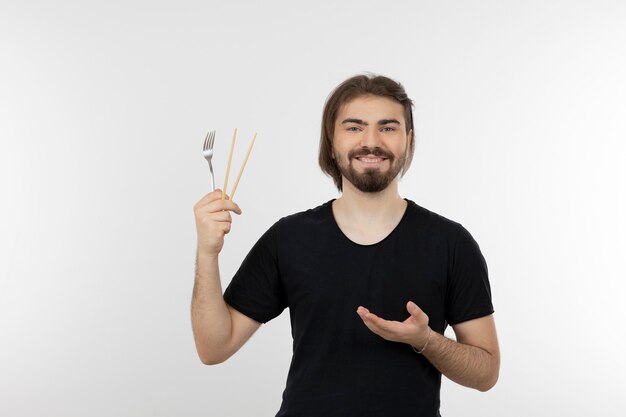 Image of bearded man holding fork over a white wall.