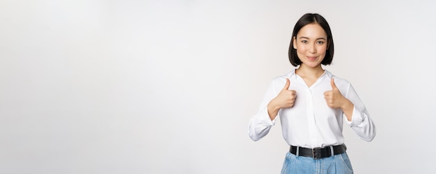 Immagine di una bella donna asiatica adulta che mostra i pollici in su indossando abbigliamento formale da ufficio rec