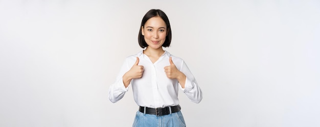 Изображение красивой взрослой азиатской женщины, показывающей большие пальцы в формальной офисной университетской одежде