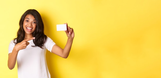 Free photo image of beautiful africanamerican woman in white tshirt pointing at credit card and smiling recomme