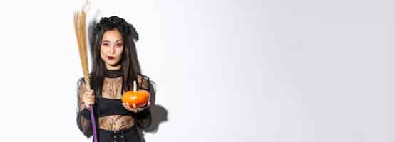 Free photo image of beautiful asian woman dressedup as a witch for halloween party holding broom and pumpkin st