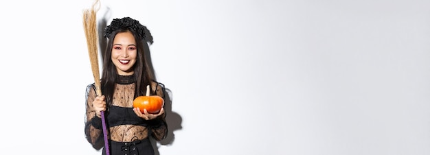 Free photo image of beautiful asian woman dressedup as a witch for halloween party holding broom and pumpkin st