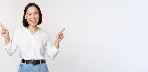 Image of beautiful asian woman pointing fingers left and right making decision showing two variants choices standing over white background