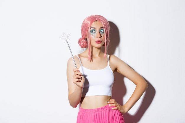 Image of beautiful female with pink wig and bright makeup, holding magic wand, cosplay fairy for halloween party, standing.