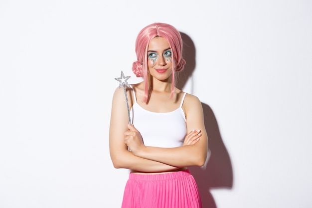 Image of beautiful girl dressed as a fairy in pink wig, holding magic wand and smiling, celebrating halloween.