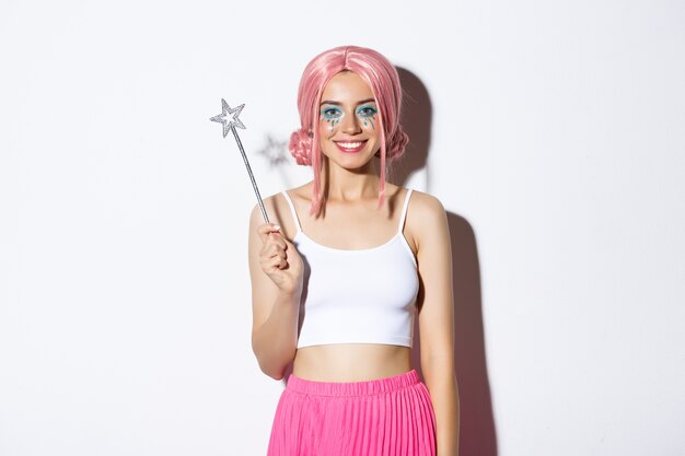 Image of beautiful girl dressed-up as a fairy for halloween party, holding magic wand and smiling, standing.