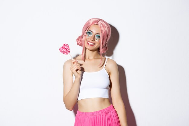 Image of beautiful girl with pink wig and bright makeup, holding candy, trick or treating on halloween in fairy costume, standing.