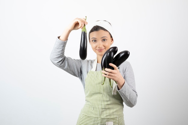 Image of beautiful housewife in apron showing fresh eggplants