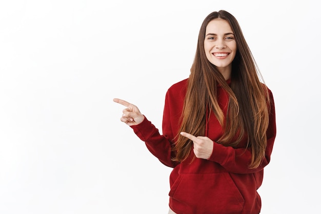 Free photo image of beautiful lady with long natural healthy hair hairdo flying in air while woman pointing aside showing haircare beauty advertisement point at logo standing over white background