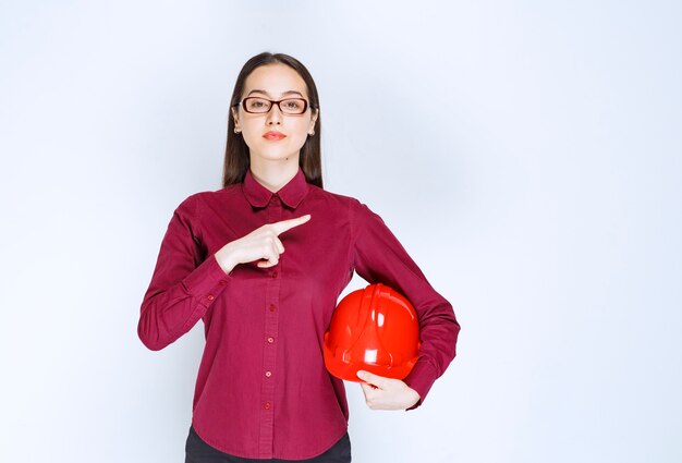 Image of beautiful woman in glasses holding crash helmet and pointing finger aside. 