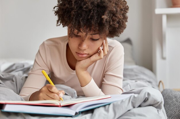 Image of beautiful woman with Afro hairstyle rewrites information in notebook from book