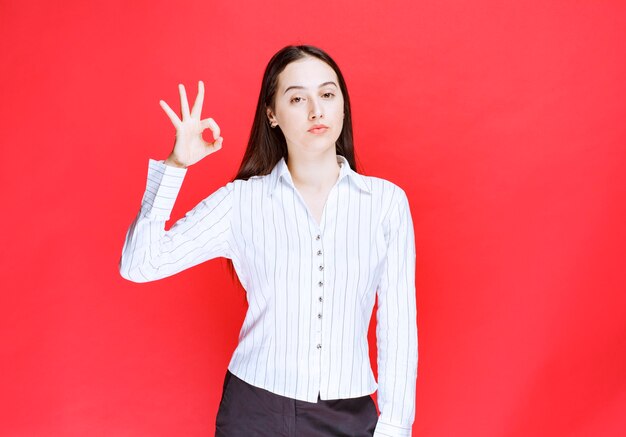 Image of beautiful young woman in formal outfit looking at camera and giving ok sign. 