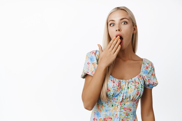 Image of blond girl looking surprised cover opened mouth gossiping standing over white background