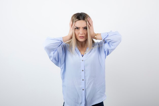 Image of blonde beautiful woman holding her head on white wall.