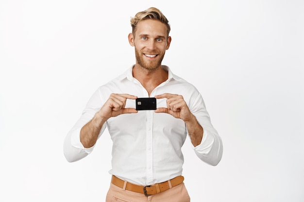 Free photo image of business guy showing credit card smiling and looking pleased standing against white background