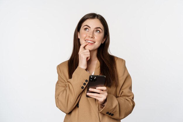 Image of businesswoman smiling using mobile phone and thinking making choice in smartphone app stand...